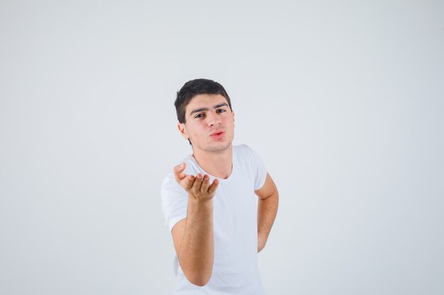 Varón joven posando mientras mira a la cámara, estirando la mano en la camiseta y mirando confiado. vista frontal.