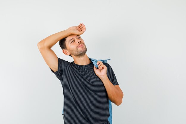 Varón joven posando mientras sostiene la chaqueta en la espalda en una camiseta y se ve lindo