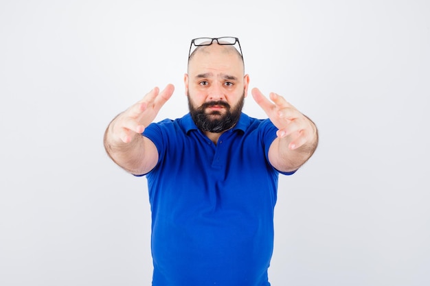 Varón joven que estira las manos hacia adelante para abrazar en camisa azul, vista frontal de gafas.