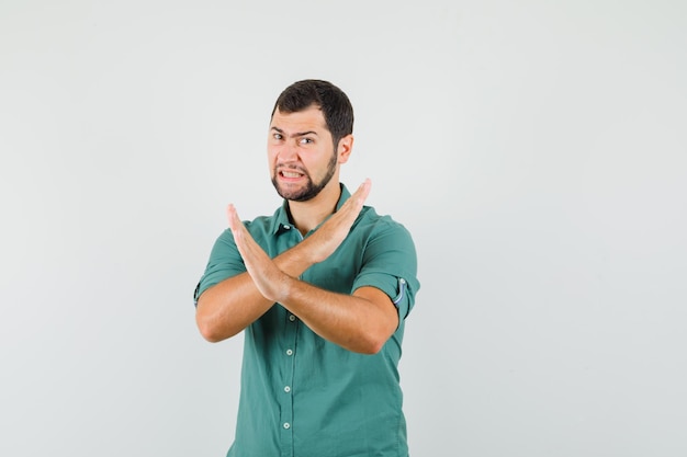 Varón joven que muestra gesto cerrado en camisa verde y que parece enojado. vista frontal.