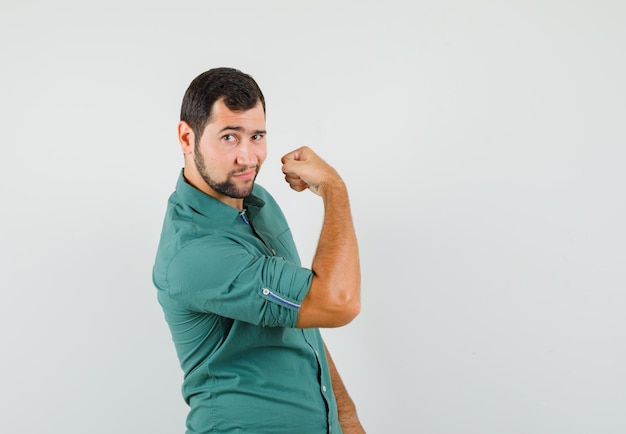 Varón joven que muestra el músculo del brazo en camisa verde y se ve guapo, vista frontal.
