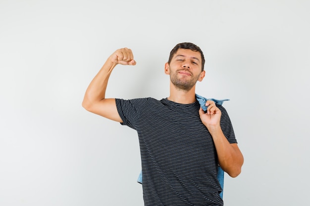 Foto gratuita varón joven que muestra los músculos del brazo sosteniendo la chaqueta en la camiseta y mirando confiado