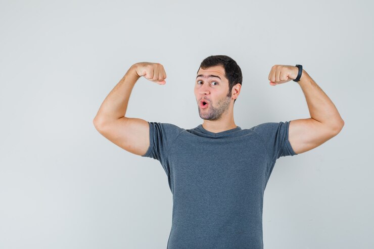 Foto gratuito varón joven que muestra los músculos de los brazos en camiseta gris y parece poderoso
