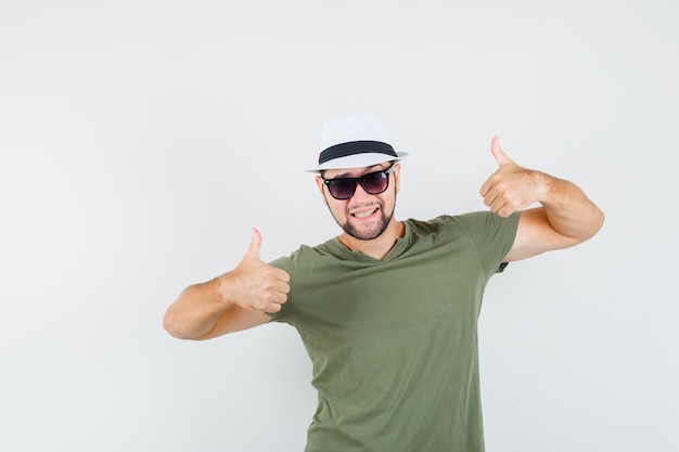 Varón joven que muestra los pulgares para arriba en la camiseta verde y el sombrero y parece optimista