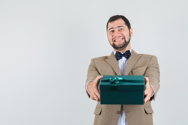 Varón joven que presenta la caja de regalo en traje y parece feliz. vista frontal.