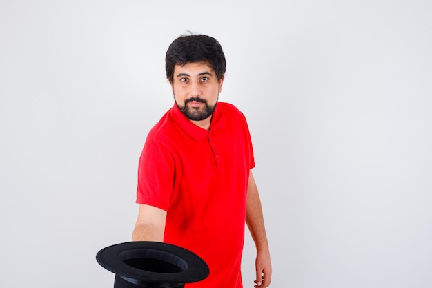 Varón joven que se quita el sombrero mientras se reúne con alguien en la vista frontal de la camiseta roja.