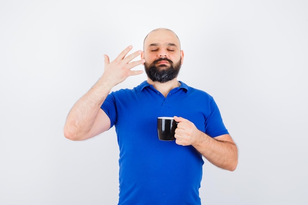 Varón joven que siente un olor fresco en la camisa azul y que parece satisfecho, vista frontal.