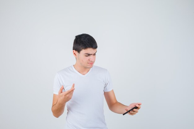 Varón joven que sostiene el teléfono mientras apunta a un lado en la camiseta y mira enfocado. vista frontal.