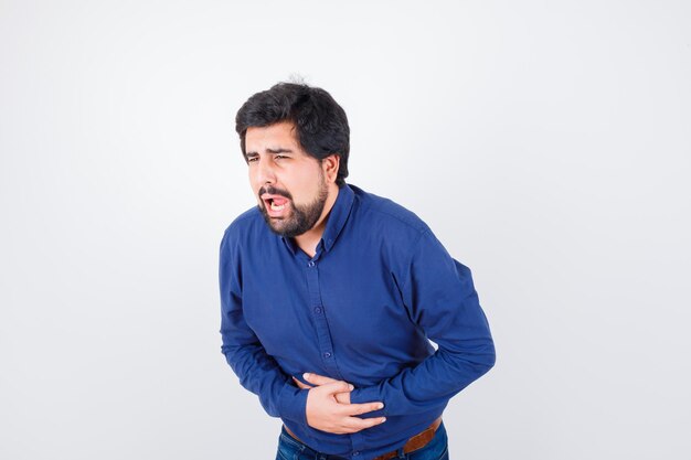 Varón joven que sufre de dolor de estómago en camisa azul y se ve mal, vista frontal.