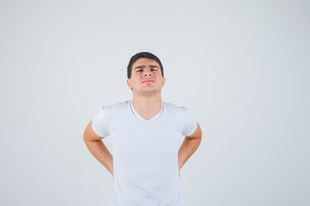 Varón joven que sufre de dolor lumbar en camiseta y se ve mal, vista frontal.