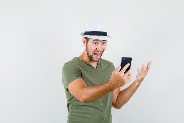 Varón joven que tiene video chat en camiseta verde y sombrero y mirando asombrado