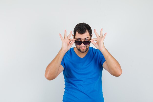 Varón joven quitándose las gafas en camiseta azul y luciendo bien