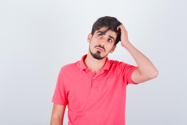 Varón joven rascándose la cabeza en camiseta y mirando pensativo, vista frontal.