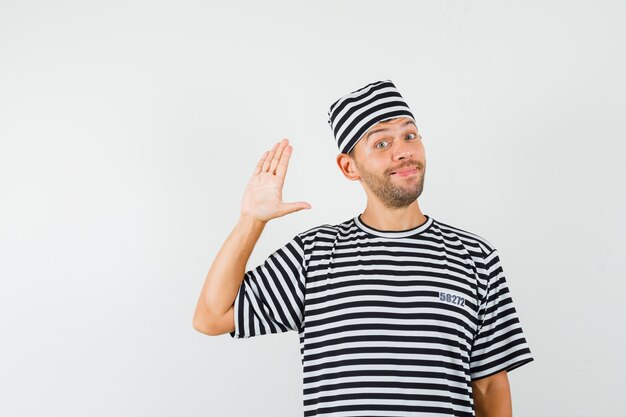 Varón joven con sombrero de camiseta a rayas agitando la mano para saludar y mirar alegre