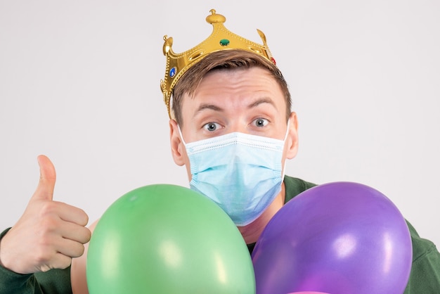 Varón joven sosteniendo globos de colores en máscara en blanco