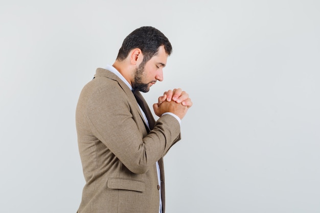 Foto gratuita varón joven sosteniendo las manos juntas en gesto de oración en traje y mirando tranquilo.