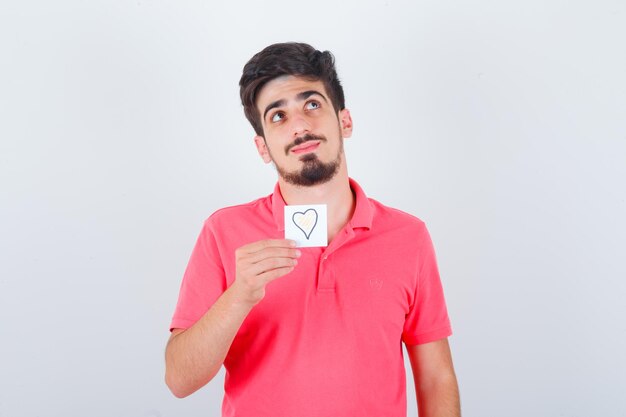 Varón joven sosteniendo una nota adhesiva en camiseta y mirando esperanzado, vista frontal.
