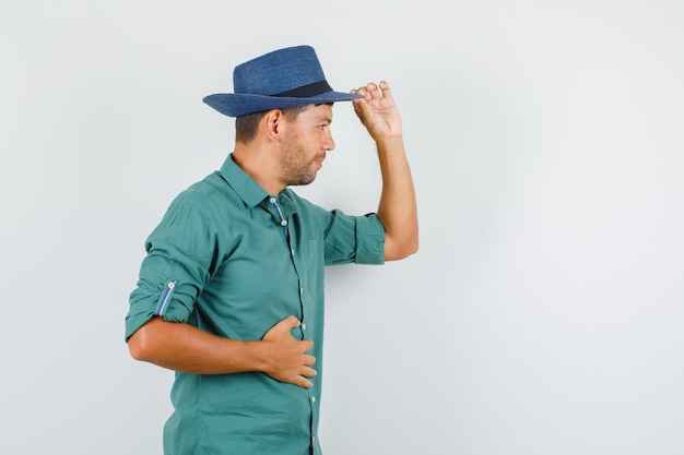 Varón joven sosteniendo sombrero y sonriendo en camisa