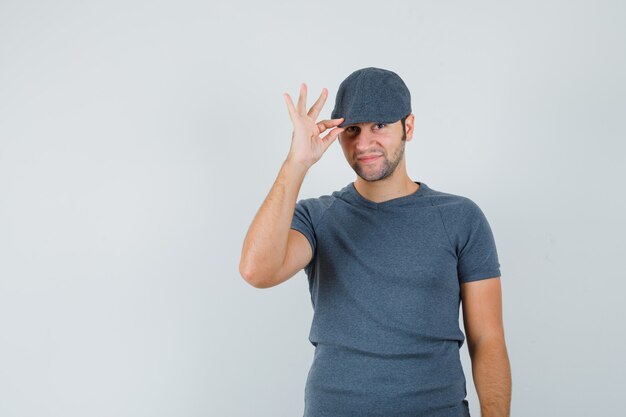 Varón joven sosteniendo su gorra en camiseta gris y luciendo elegante