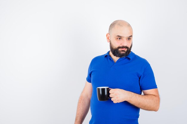 Varón joven sosteniendo la taza mientras mira a un lado en la vista frontal de la camisa azul.