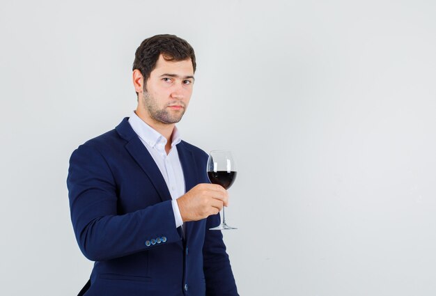 Varón joven sosteniendo un vaso de bebida alcohólica en traje y mirando tranquilo. vista frontal.