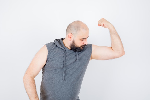 Foto gratuita varón joven en sudadera con capucha sin mangas que muestra los músculos del brazo y mirando confiado, vista frontal.