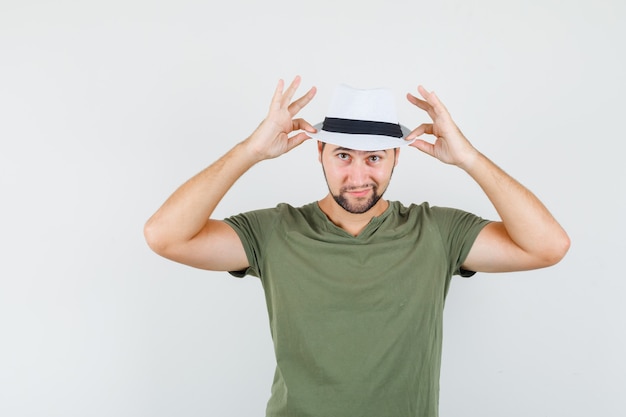 Varón joven tocando su sombrero en camiseta verde y luciendo bien