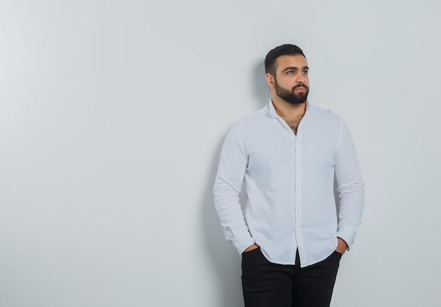 Foto gratuita varón joven tomados de la mano en los bolsillos con camisa blanca, pantalones y aspecto elegante