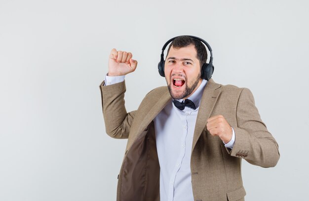 Varón joven en traje disfrutando de la música con auriculares y mirando juguetón, vista frontal.