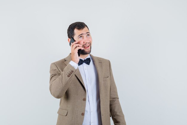 Varón joven en traje hablando por teléfono móvil y mirando alegre, vista frontal.