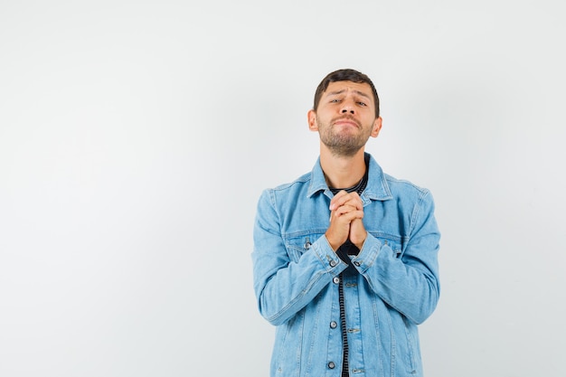 Foto gratuita varón joven uniendo las manos en gesto de oración en la chaqueta de la camiseta y mirando esperanzado