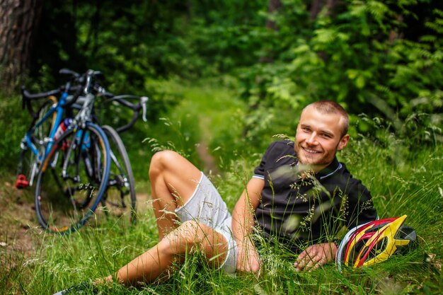 Varón positivo descansando sobre un césped después de andar en bicicleta.