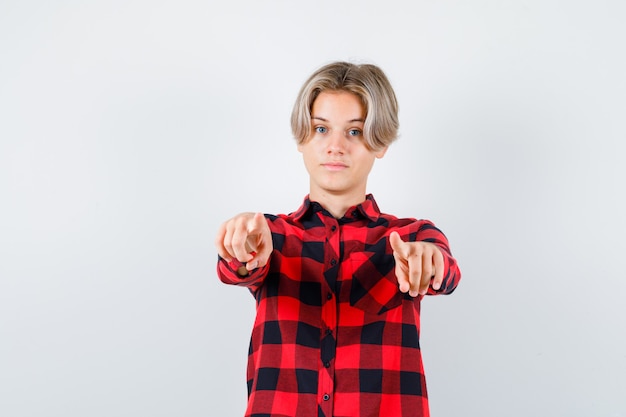 Foto gratuita varón rubio adolescente apuntando al frente en camisa casual y mirando confiado. vista frontal.