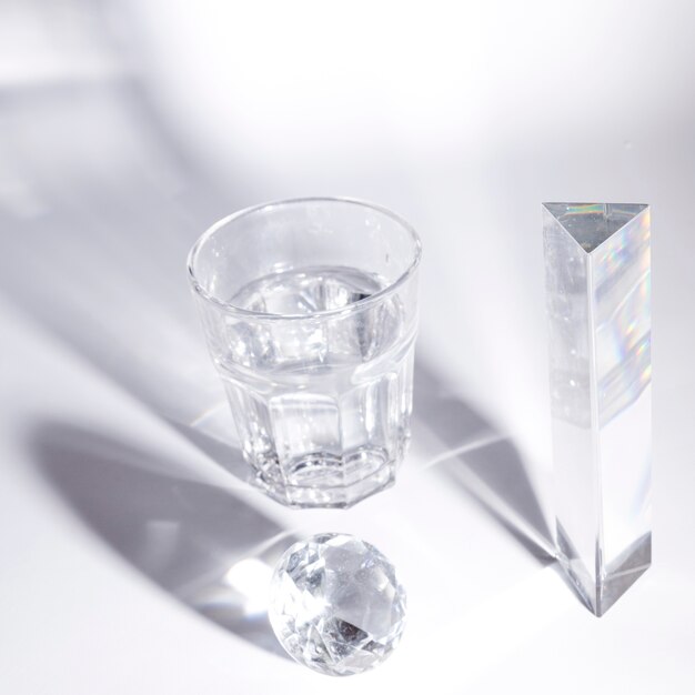Vaso de agua y cristal de diamante y prisma con sombra oscura sobre fondo blanco