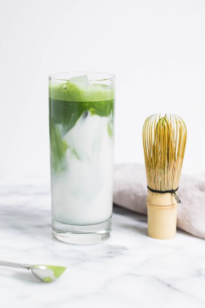 Vaso de agua con hojas de vegetales sobre una superficie blanca