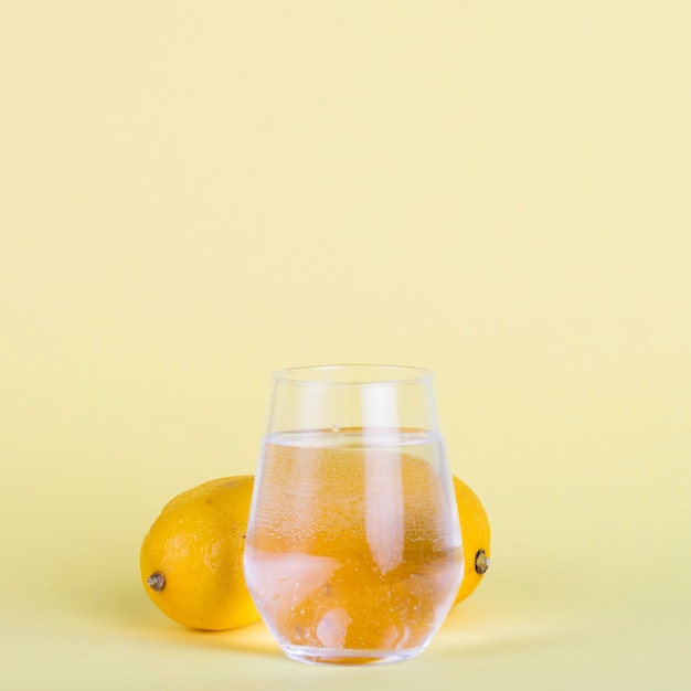 Vaso de agua y limones sobre fondo amarillo