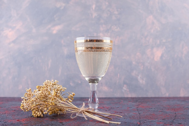 Un vaso de agua mineral con flor seca colocada sobre un fondo oscuro.