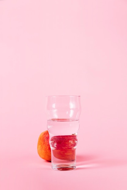 Vaso de agua y nectarina sobre fondo rosa