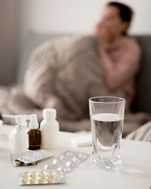 Foto gratuita vaso de agua y pastillas con persona borrosa enferma