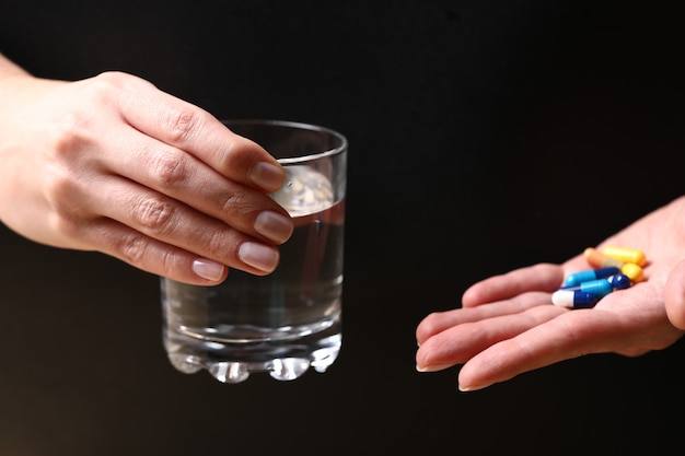 Un vaso de agua y píldoras médicas en manos de una persona.