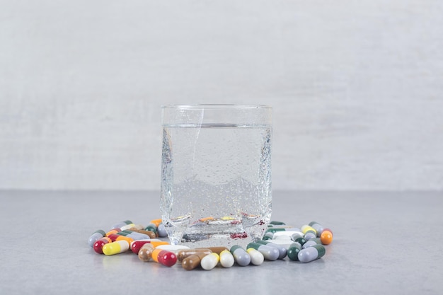 Un vaso de agua pura con pastillas de colores sobre fondo gris.