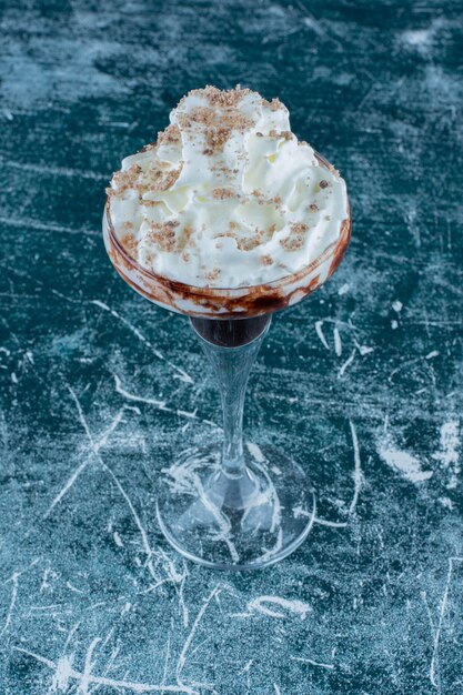 Un vaso batido con crema sobre fondo azul. Foto de alta calidad