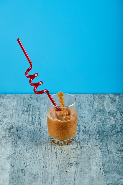 Un vaso de batido fresco con paja sobre mesa gris.