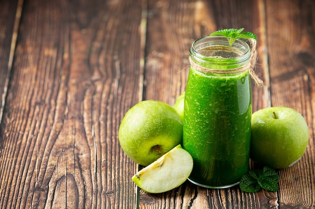 Vaso de batido saludable de manzana verde junto a manzanas verdes frescas