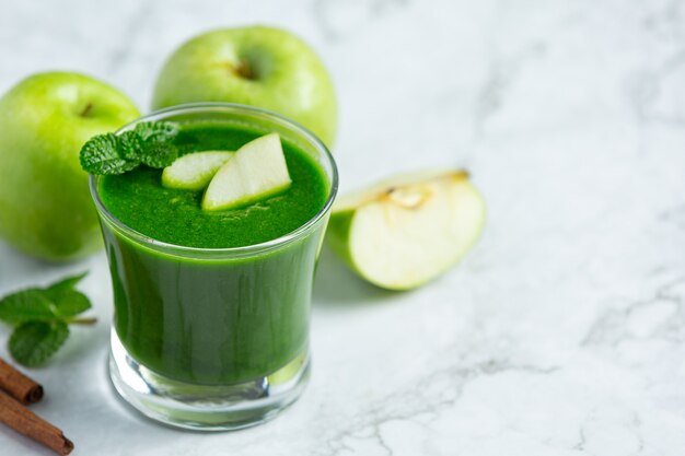 Vaso de batido saludable de manzana verde junto a manzanas verdes frescas