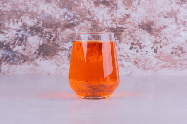 Un vaso de bebida de naranja sobre mármol.