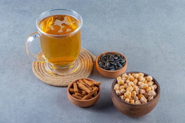 Foto gratuita vaso de bebida sobre un salvamanteles junto al cuenco de garbanzos, picatostes y semillas, sobre la superficie de mármol.