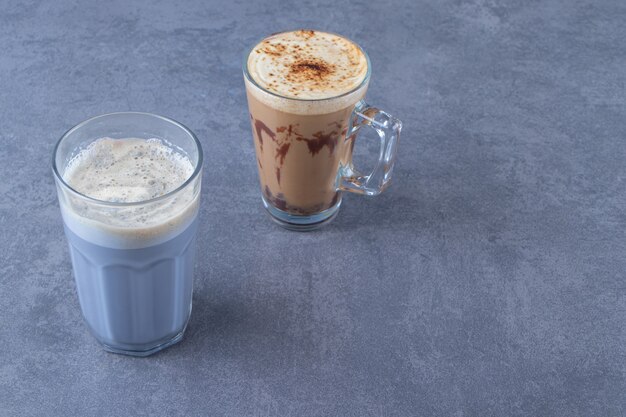 Un vaso de café azul junto al capuchino de chocolate, sobre la mesa azul.