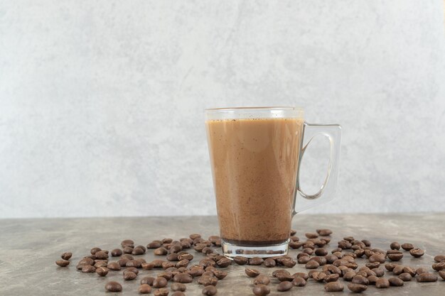 Vaso de café caliente y granos de café en la mesa de mármol