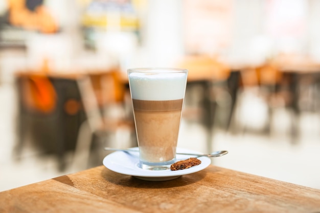 Vaso de café capuchino con cuchara en mesa de madera